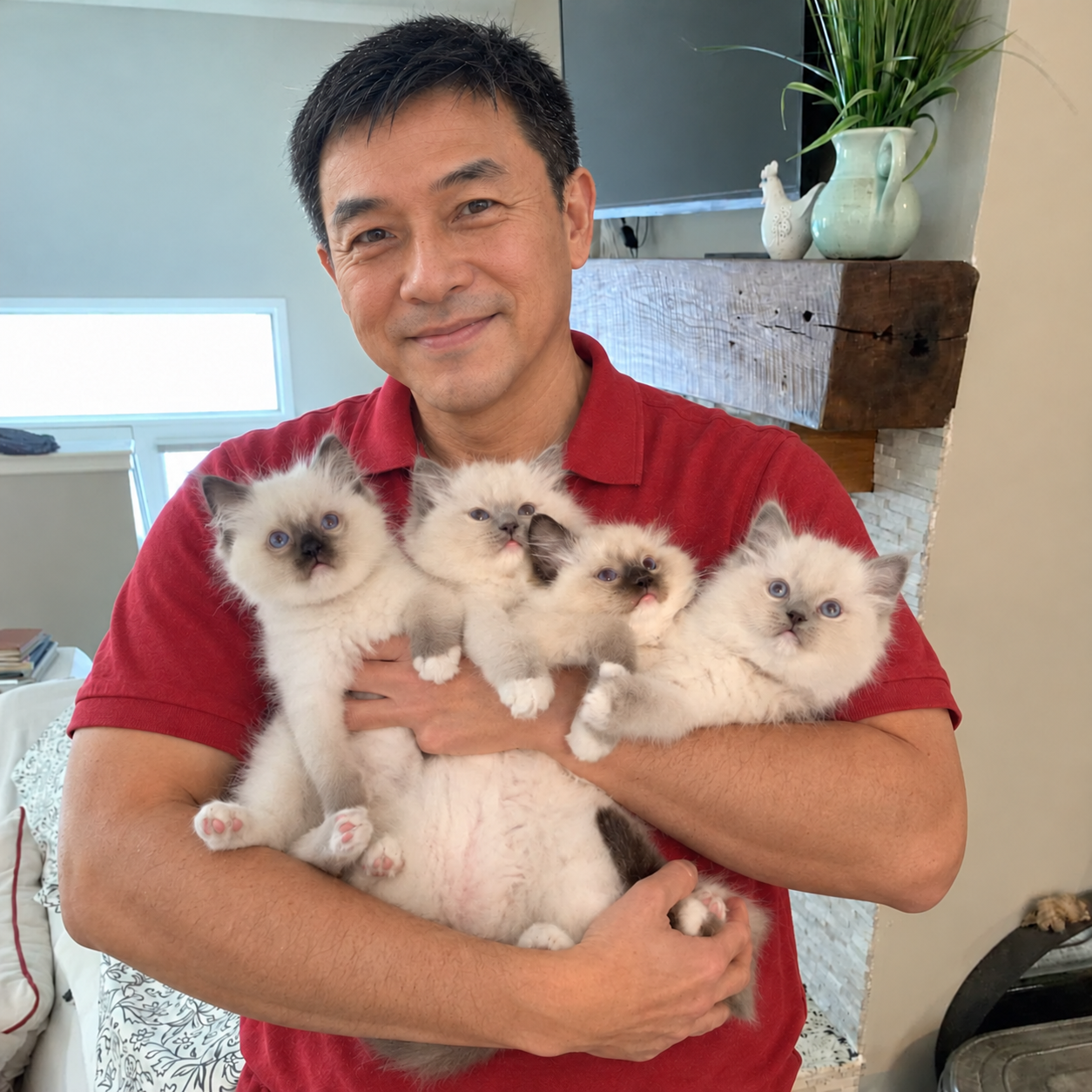 A man in a red shirt holding four fluffy kittens at home